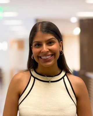 Zenia smiling in a cream top, standing in a bright hallway.