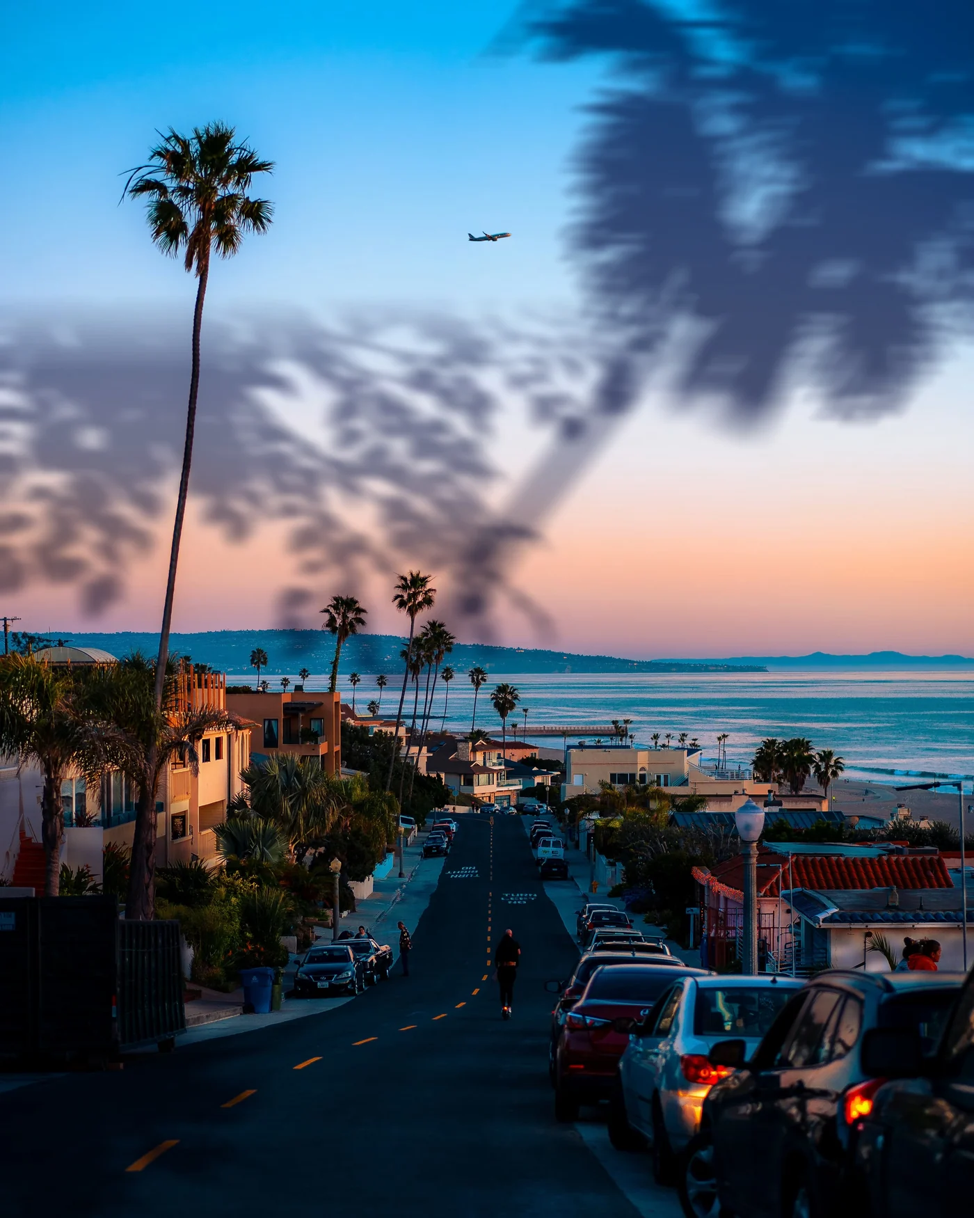 A coastal street at sunset lined with palm trees, with palm-leaf shadows falling across the top of the photo.