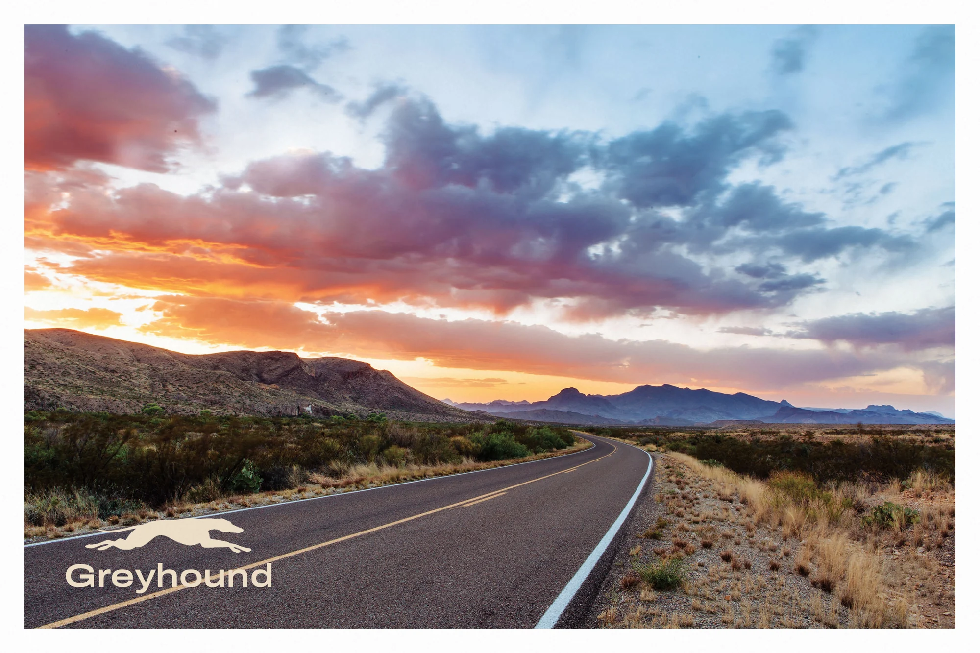 A postcard front: a desert highway at sunset under a dramatic sky, with a small cream Greyhound logo in the corner.